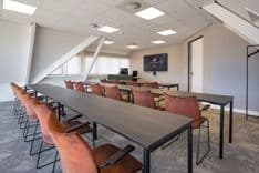 Harry Frens kamer in cursusopstelling voor 16 personen met tafels, stoelen, 75-inch scherm en ramen met daglicht — Mudde Kok FlexCentre