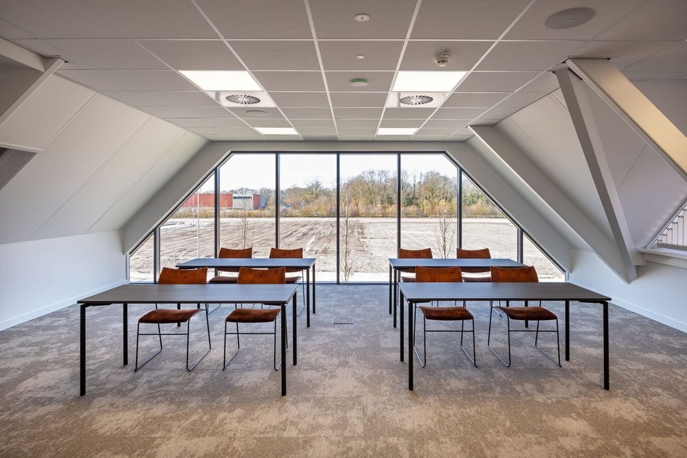 Harry Frens kamer in cursusopstelling met rijen tafels en stoelen richting 75-inch scherm, ramen en uitzicht achterzijde — Mudde Kok FlexCentre