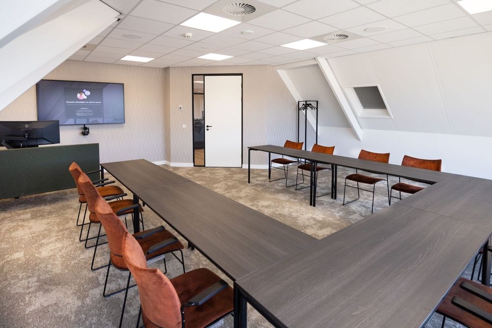 Harry Frens kamer in cursusopstelling voor 12 personen met tafels, stoelen, 75-inch scherm en ramen met daglicht — Mudde Kok FlexCentre