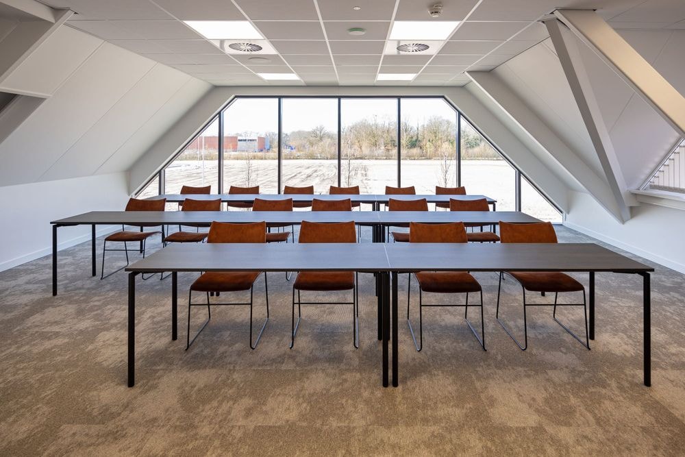 Harry Frens kamer in cursusopstelling voor 16 personen met tafels, stoelen, 75-inch scherm en ramen met daglicht — Mudde Kok FlexCentre