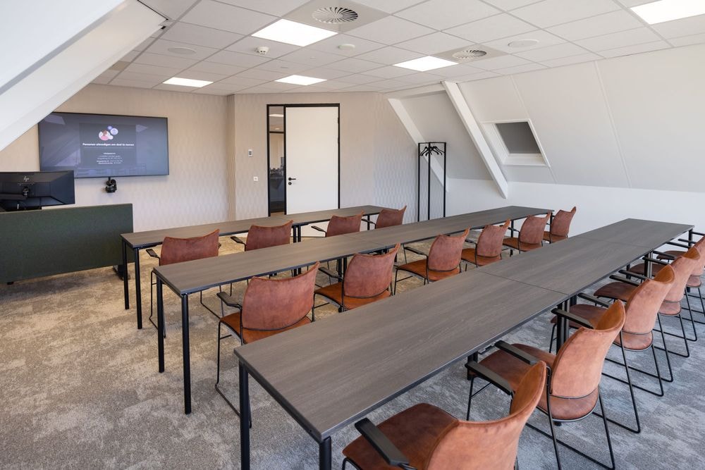 Harry Frens kamer in cursusopstelling voor 16 personen met tafels, stoelen, 75-inch scherm en ramen met daglicht — Mudde Kok FlexCentre