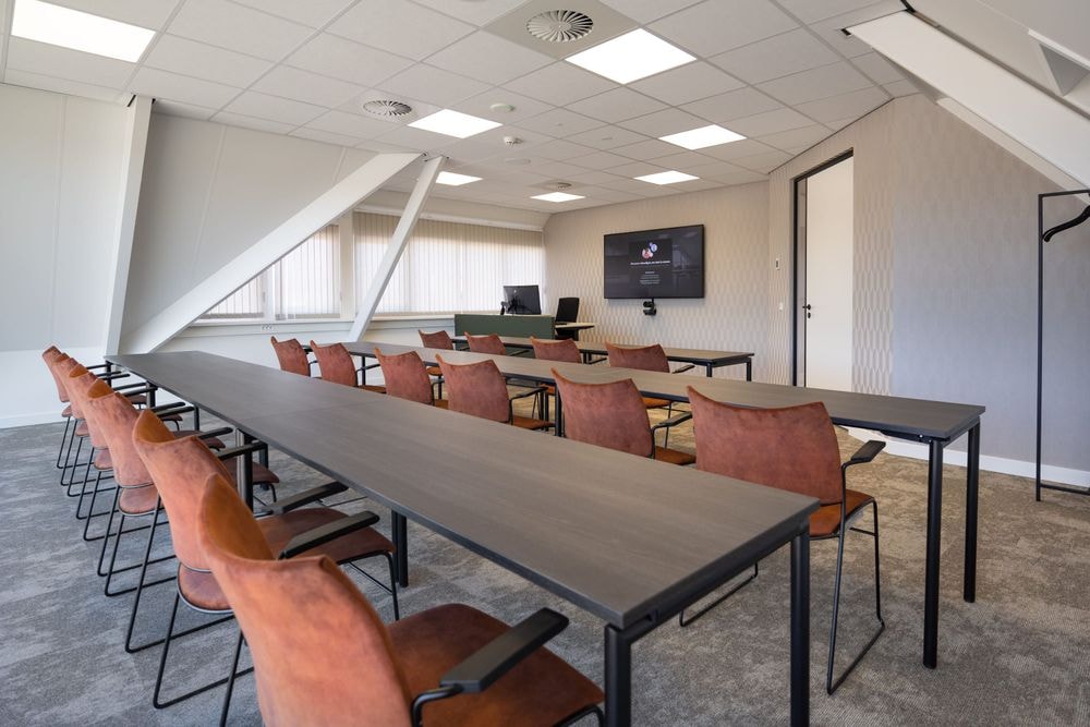 Harry Frens kamer in cursusopstelling voor 16 personen met tafels, stoelen, 75-inch scherm en ramen met daglicht — Mudde Kok FlexCentre