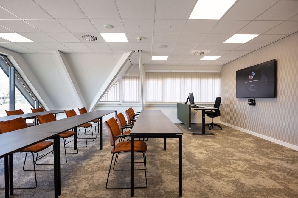 Harry Frens kamer in cursusopstelling voor 16 personen met tafels, stoelen, 75-inch scherm en ramen met daglicht — Mudde Kok FlexCentre