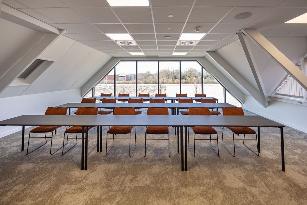 Harry Frens kamer in cursusopstelling voor 18 personen met tafels, stoelen, 75-inch scherm en ramen met daglicht — Mudde Kok FlexCentre