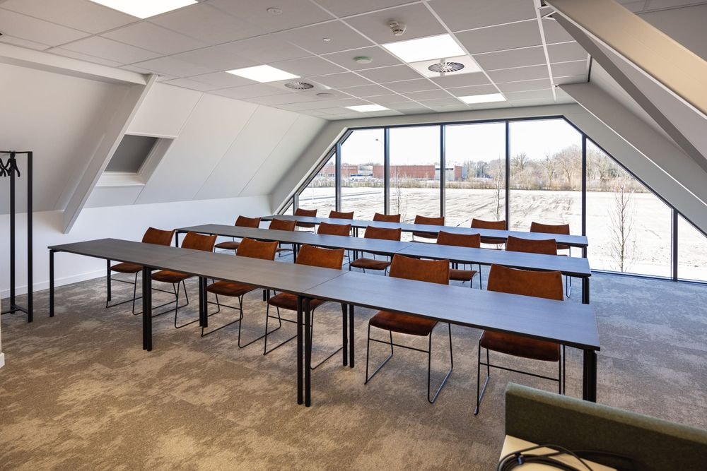 Harry Frens kamer in cursusopstelling voor 18 personen met tafels, stoelen, 75-inch scherm en ramen met daglicht — Mudde Kok FlexCentre