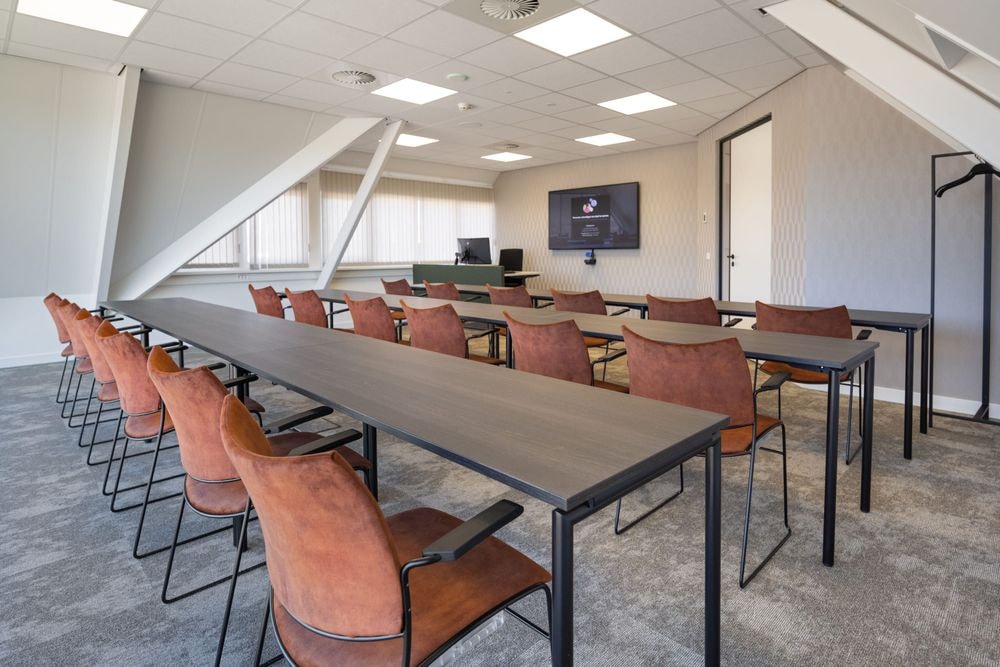 Harry Frens kamer in cursusopstelling voor 18 personen met tafels, stoelen, 75-inch scherm en ramen met daglicht — Mudde Kok FlexCentre