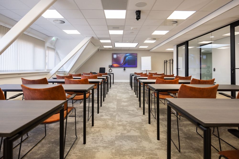 Huib van de Vecht zaal in cursusopstelling voor 30 personen met vaste werkplekken en scherm — Mudde Kok FlexCentre