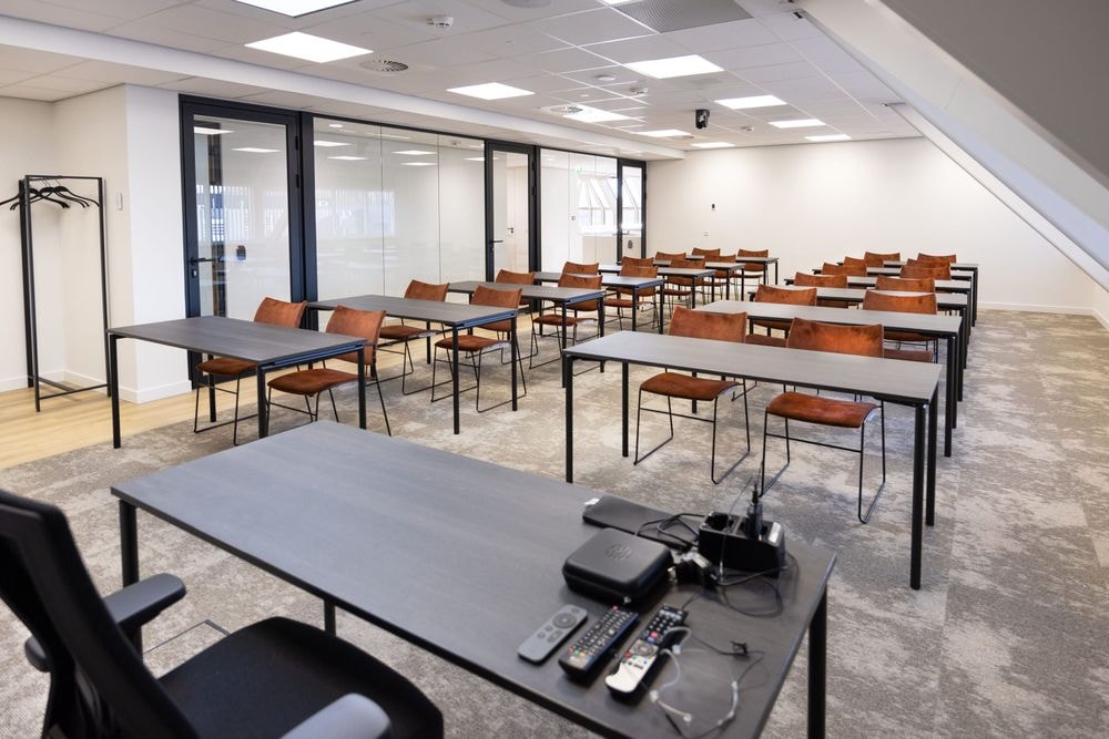 Huib van de Vecht zaal in cursusopstelling voor 16 personen met vaste werkplekken en scherm — Mudde Kok FlexCentre